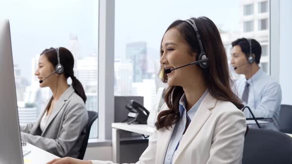 Asian woman customer service operators talking on headsets and using computer at call center