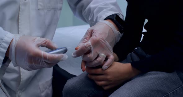 Young Asian male doctor measuring blood sugar level of boy with glucometer 4k alt