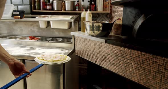 Preparing pizza in the kitchen in the restaurant. Pizza is placed in the oven alt
