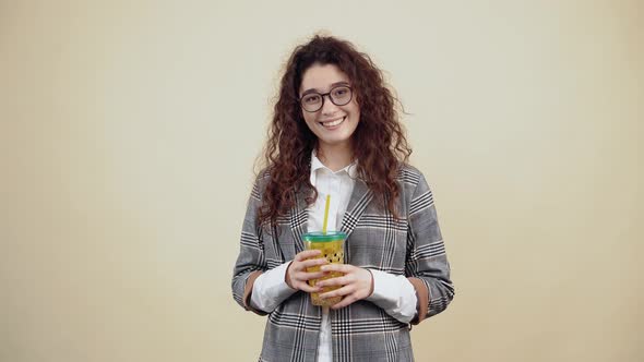 The Curlyhaired Teenager Smiles with Her Teeth Out While Holding a Yellow Glass of Fresh Juice alt