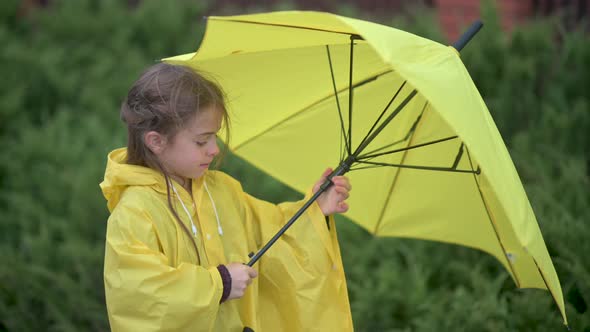 girl in a yellow raincoat folds her umbrella in rainy weather in the autumn park.