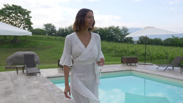 A woman walking with a glass of white wine at a pool traveling at a luxury resort in Italy, Europe alt