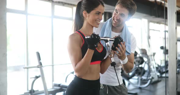 Beautiful Woman Doing Exercises with Personal Trainer in Gym