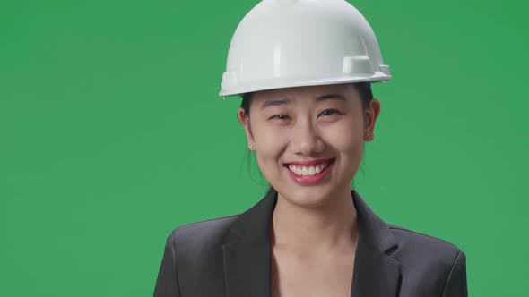 Close Up Of Asian Female Engineer With Safety Helmet Smiling In The Green Screen Studio alt