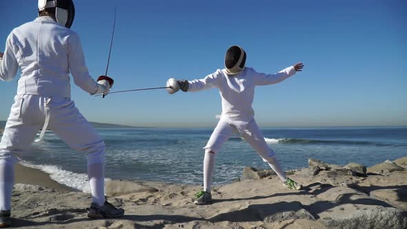A man and woman fencing on the beach alt