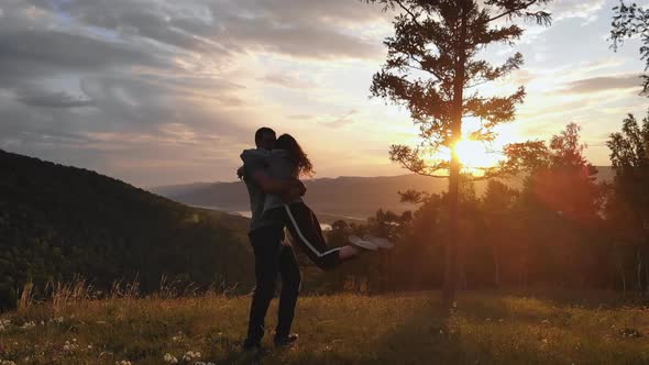Couple of Young People in Love at Sunset. A Woman in the Arms of Her Man on Top of a Mountain