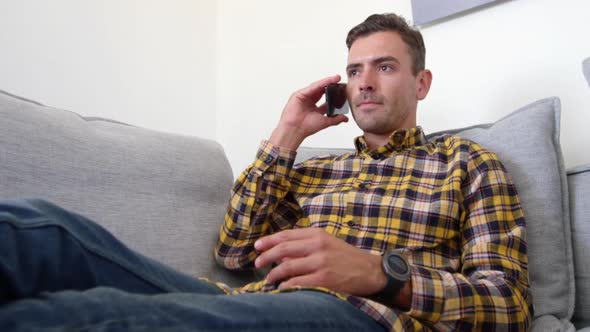 Young man talking on mobile phone in living room at home 4k