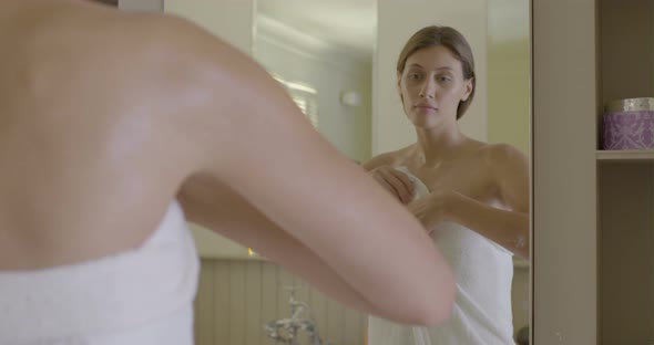 Woman wrapped in towel, looking into mirror and touching skin