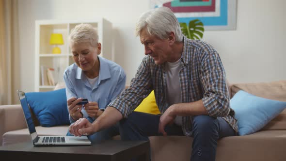 Happy Mature Couple Sitting on Sofa and Doing Online Shopping on Laptop alt