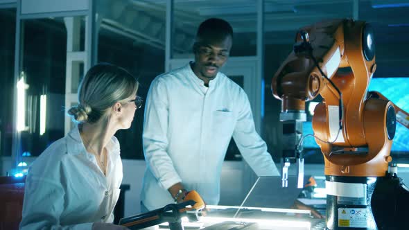 African Engineer and His Female Colleague Are Working with a Robot alt