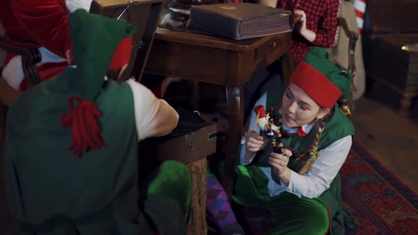 Fairy characters in green costumes play with a toy at Christmas. Happy female elf holding a toy alt
