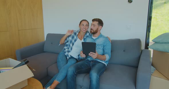 Happy Couple Renters Owners Tenants Sit on Sofa Use Digital Tablet on Moving Day in New House, Man alt