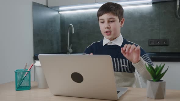 Smiling Boy Chatting Online By Video Call with Laptop Computer at Home While Sitting at the Table alt