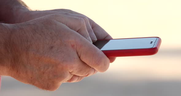 Close up of hands of one mature man using and holding a red phone.