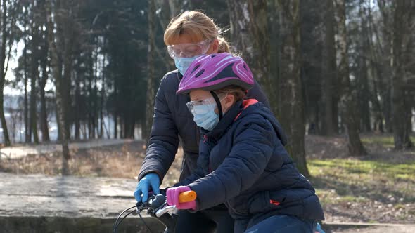 Mom teaches her daughter to ride a bike in the city Park. they are wearing protective helmets