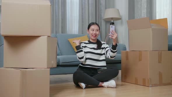 Asian Woman With Cardboard Boxes Live Stream By Smartphone After Moving Into A New House  alt