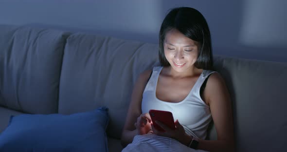 Woman use of smart phone and sit on sofa at home in the evening alt