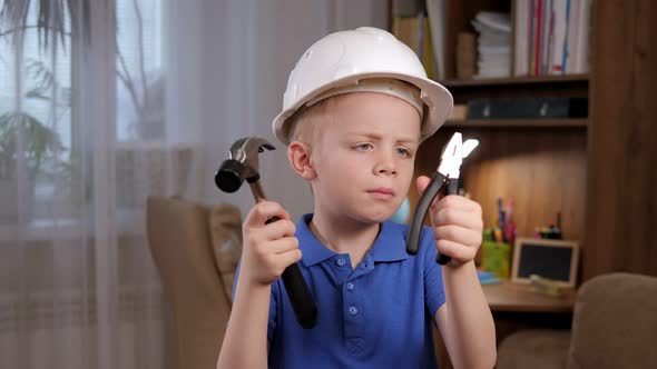 Portrait of a Small Surprised Boy in a Helmet with Tools in His Hands at Home alt