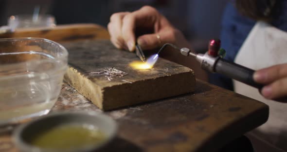 Close up of hands of caucasian female jeweller using gas burner, making jewelry alt