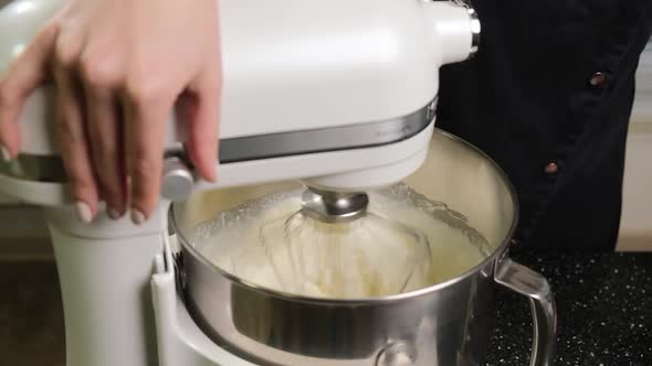 White Mixer Which is Whipping the Cream in a Stainless Bowl in the Kitchen alt