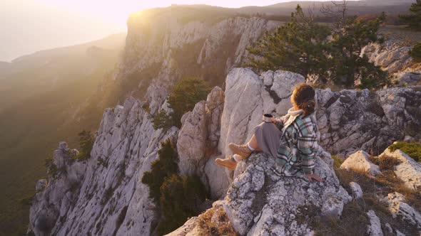 Pretty Woman Drinks Tea Sitting on Steep Cliff at Sunset