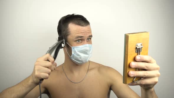 A Young Guy in a Protective Mask Cuts His Own Hair with an Electric Trimmer During a Pandemic