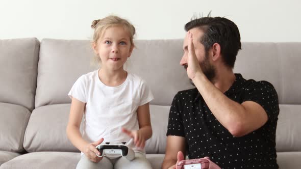 Father and His Cute Little Daughter are Playing Game Console and Smiling While Sitting on Couch