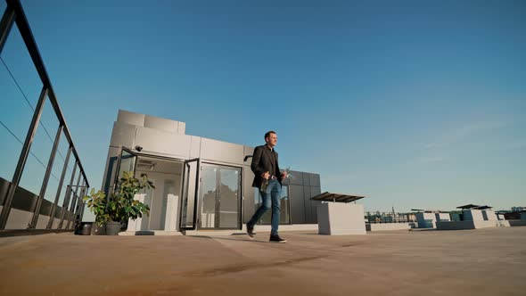 Man Carries a Bottle of Champagne at the Setting Sun on the Roof of a Skyscraper