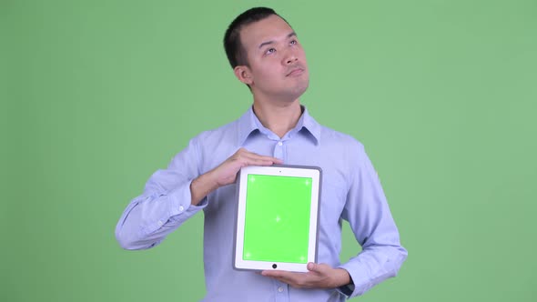 Happy Asian Businessman Thinking While Showing Digital Tablet alt