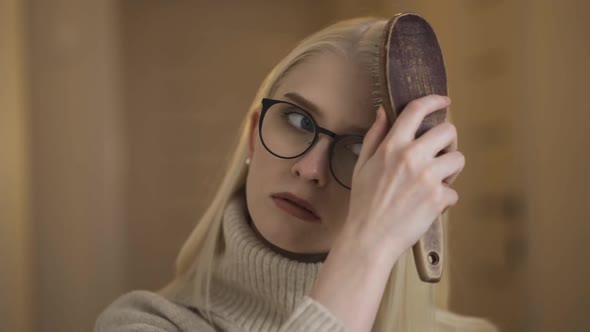 Young Beautiful Woman in Glasses is Combing with a Wooden Comb