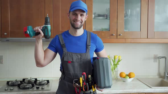 Repairman Holds a Screwdriver and a Suitcase of Tools in the Kitchen and Looks at the Camera alt