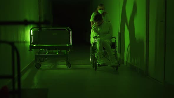 A Paramedic is Driving a Mad Male Patient in Wheelchair Down Corridor in Mental Hospital alt
