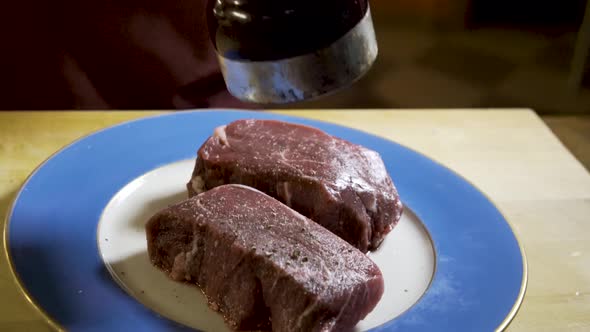 As camera slides from right to left, a chef grinds fresh black pepper onto two large pieces of raw, alt