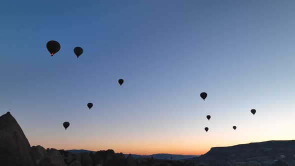 Hot air balloons fly over the mountainous landscape of Cappadocia, Turkey. alt