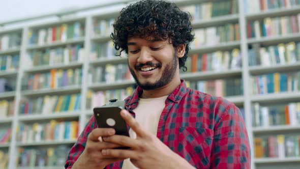 Happy Indian or Arabian Millennial Guy Freelancer or Student Using His Smartphone Chatting with alt