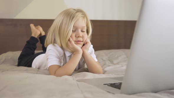 a Cute Schoolboy Lying on the Bed and Watching a Video on a Laptop. Distance Learning Online