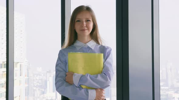 Business Woman Holding the Folder with Documents Near Window with City View alt