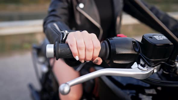 Closeup of Female Hand Twists Accelerometer Lever on Classic Black Retrostyled Motorcycle While alt