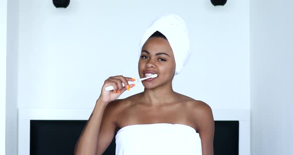 Young black woman cleaning teeth with toothbrush smiling to camera.
