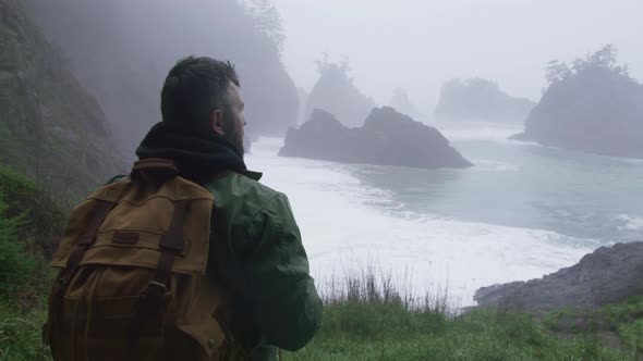 Back View of Handsome Man with Tourist Backpack Enjoying Cinematic Oregon Beach alt