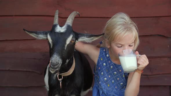 The Girl Drinks Goat Milk From a Mug and Hugs Her Beloved Goat. alt