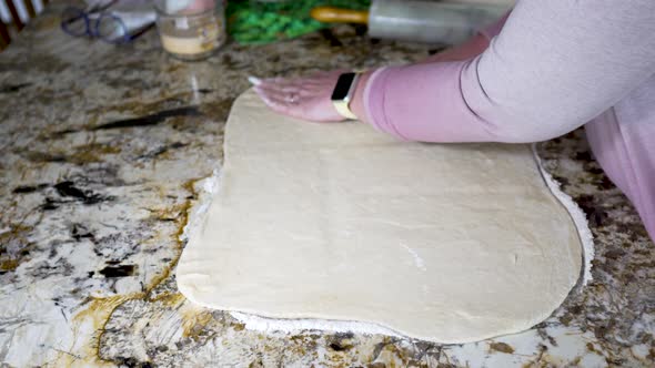 Squaring up the sides of rolled out dough to make cinnamon rolls - isolated side view alt