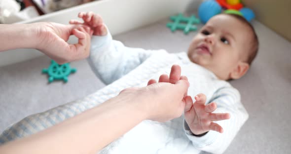 Happy Mother Lifting Baby Helps Son Sit Down Lying on Bed at Home alt
