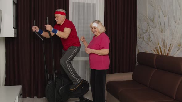Active Senior Mature Grandfather Man in Sportswear Using Orbitrek Grandma Encourages Him at Home alt