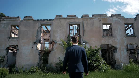 Successful man in a jacket goes to an abandoned ruined house alt