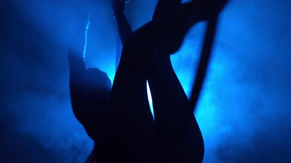 Silhouette Aerial Gymnast Performs Trick in Ring in Smoky Room with Backlit alt