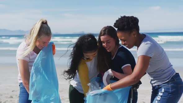 Diverse group of female friends putting rubbish in refuse sacks at the beach alt