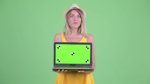 Happy Young Blonde Tourist Woman Showing Laptop and Looking Surprised alt