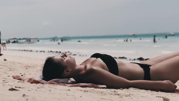 Young Woman Sunbathes on a Paradise Sandy Beach Lying in Black Bikini Near Ocean alt