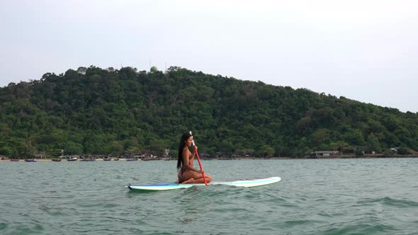 Young Woman In Bikini Kneeling On And Rowing Paddle Board In Sea alt